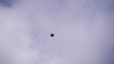 Kırmızı ve mavi bir uçurtma, beyaz bir gökyüzünde yavaşça aşağı ve yukarı uçuyor. Uçurtmanın yakın çekim görüntüsü..