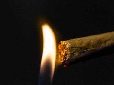 Siyah arka planda alevlerle izole edilmiş rulo sigaranın makro çekimi.