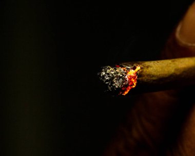 Yanmış sigaranın makro çekimi siyah arka planda küçük bir alevle izole edilmiş..