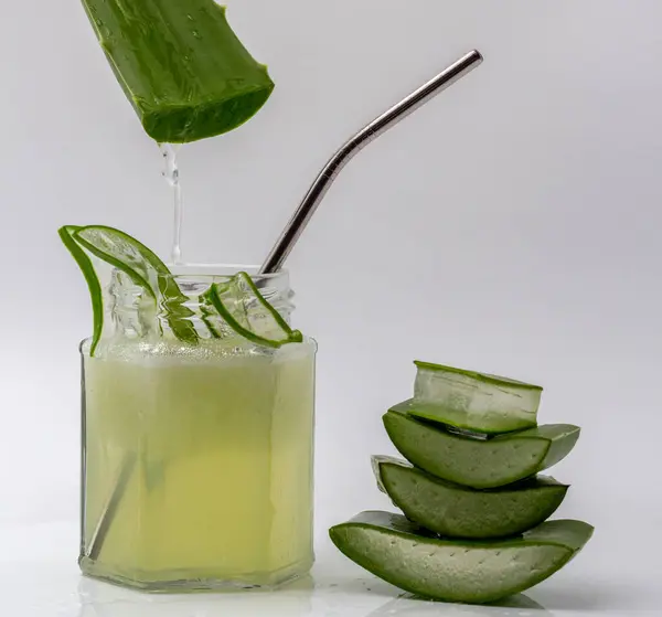 stock image Aloe vera gel dripping on a jar of aloe vera juice with sliced and stacked aloe vera isolated on white background.