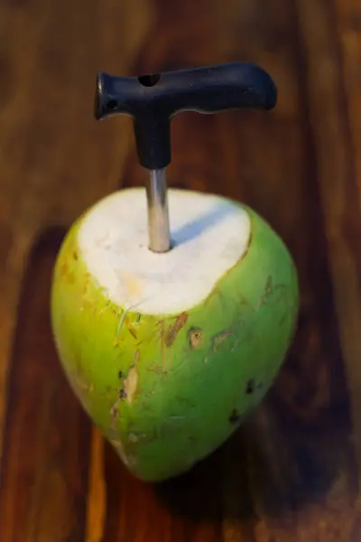 stock image A close-up photo of a tender coconut with a coconut opener against a wooden platform.