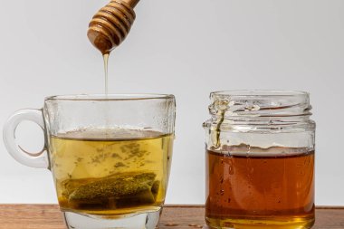 Bir kavanoz balın yanında duran yeşil çaydan damlayan bal.