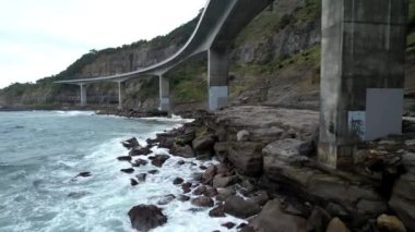 Pasifik kıyılarındaki Sea Cliff Köprüsü 'nün havadan görüntüsü Wollongong, Illawarra, Yeni Güney Galler, Avustralya. 665 metre uzunluğundaki Köprü, Büyük Pasifik Yolu boyunca önemli bir noktadır. Köprü Wollongong halkı ve dünya için bir ikondur..