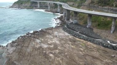 Pasifik kıyılarındaki Sea Cliff Köprüsü 'nün havadan görüntüsü Wollongong, Illawarra, Yeni Güney Galler, Avustralya. 665 metre uzunluğundaki Köprü, Büyük Pasifik Yolu boyunca önemli bir noktadır. Köprü Wollongong halkı ve dünya için bir ikondur..