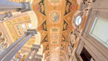 Ceiling of the Library of Congress. Intricate interior of a historic cathedral featuring towering columns, ornate arches, and a painted ceiling filled with golden frescoes and geometric motifs.