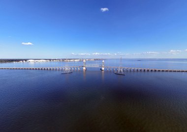 James River Lift Köprüsü JRB, yüksek kuleler ve görünür kablolarla desteklenen sakin bir su geçidini kapsar. Bu altyapı uzak kıyıları birbirine bağlıyor, parlak ve berrak bir gökyüzünün altındaki mavi suyu yansıtıyor.