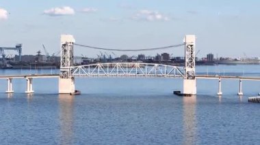 James River Lift Köprüsü JRB, yüksek kuleler ve görünür kablolarla desteklenen sakin bir su geçidini kapsar. Bu altyapı uzak kıyıları birbirine bağlıyor, parlak ve berrak bir gökyüzünün altındaki mavi suyu yansıtıyor.