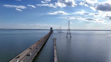 James River Lift Köprüsü JRB, yüksek kuleler ve görünür kablolarla desteklenen sakin bir su geçidini kapsar. Bu altyapı uzak kıyıları birbirine bağlıyor, parlak ve berrak bir gökyüzünün altındaki mavi suyu yansıtıyor.