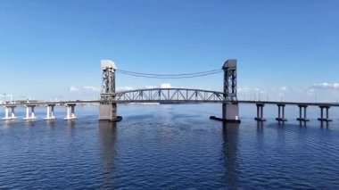 James River Lift Köprüsü JRB, yüksek kuleler ve görünür kablolarla desteklenen sakin bir su geçidini kapsar. Bu altyapı uzak kıyıları birbirine bağlıyor, parlak ve berrak bir gökyüzünün altındaki mavi suyu yansıtıyor.