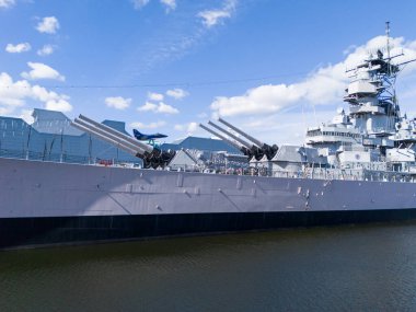 The historic Wisconsin BB-64 battleship sits docked at the Norfolk harbor, featuring multiple gun turrets, radar towers, and a towering superstructure, conveying power, defense, and maritime strength suitable for military and history themes.