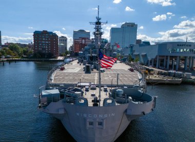 The historic Wisconsin BB-64 battleship sits docked at the Norfolk harbor, featuring multiple gun turrets, radar towers, and a towering superstructure, conveying power, defense, and maritime strength suitable for military and history themes.