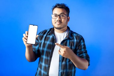 Akıllı telefon gösteren Hintli bir adamın portresi mavi arka plandaki beyaz ekrana işaret ediyor.