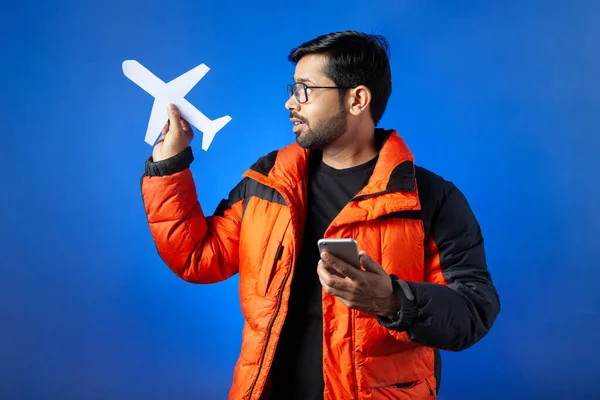 Indian ethnicity, journey, travel. A young man clutching paper cut airplane and mobile phone.