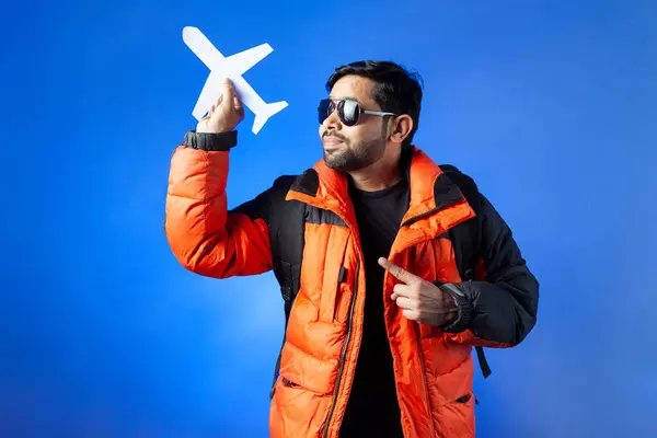 Asian and Indian ethnicity, passenger, journey. Indian man holding paper craft aeroplane and pointing with fingers.