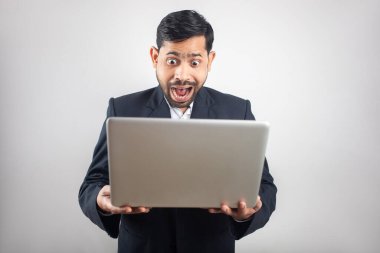 Takım elbiseli Hintli adam şaşırmış bir ifadeyle laptop ekranına bakıyor.