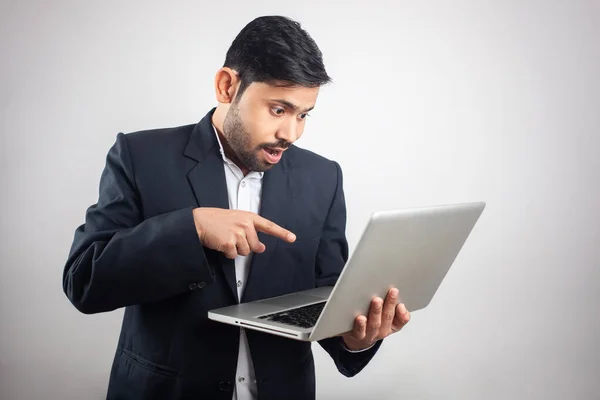 indian businessman pointing finger towards laptop screen on grey background