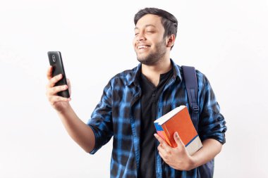 Elinde kitaplarla cep telefonu kullanırken gülümseyen genç bir çocuk.