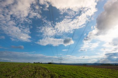 Ulaşım için elektrik direği ve bulutlu bir gökyüzünün önündeki doğal manzaralardan yüksek voltaj transferi