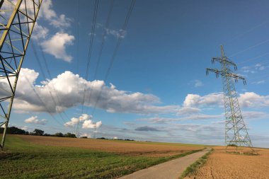 Ulaşım için elektrik direği ve bulutlu bir gökyüzünün önündeki doğal manzaralardan yüksek voltaj transferi