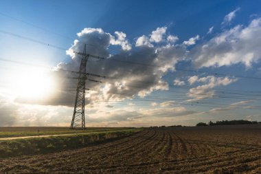 Ulaşım için elektrik direği ve bulutlu bir gökyüzünün önündeki doğal manzaralardan yüksek voltaj transferi