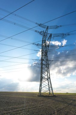 Ulaşım için elektrik direği ve bulutlu bir gökyüzünün önündeki doğal manzaralardan yüksek voltaj transferi