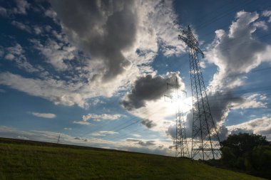 Ulaşım için elektrik direği ve bulutlu bir gökyüzünün önündeki doğal manzaralardan yüksek voltaj transferi