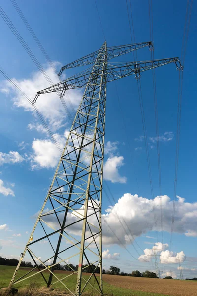 Electricity pylon for transmission and current transfer of high voltage through natural landscapes in front of a cloudy sky