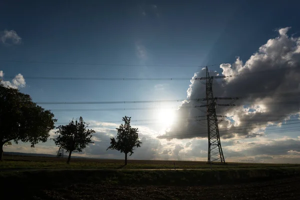 Electricity pylon for transmission and current transfer of high voltage through natural landscapes in front of a cloudy sky