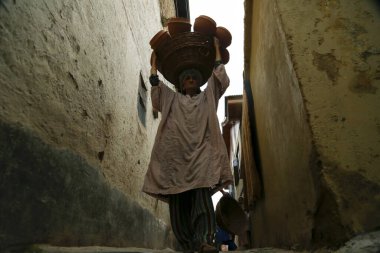 10 Ağustos 2023, Srinagar Kashmir, Hindistan: Bir kadın Srinagar 'ın eteklerindeki bir Aly' de yürürken toprak rengi Tumbaknari (bir Kashmiri müzik davulu) dolu bir sepet taşıyor. Kaşmir düğünlerinde