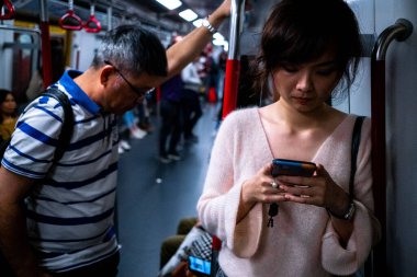 Hong Kong 'da metroda seyahat eden bir kız cep telefonunu kontrol ediyor.