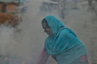 27 Kasım 2023, Srinagar Kashmir, Hindistan: Kaşmirli bir kadın Srinagar 'da kuru çin yaprağı yakıyor. Kashmiriler günümüzde ağaçlardan düşen kuru yaprakları toplar ve onları yakarak kömür üreterek yanıcı madde olarak kullanırlar.