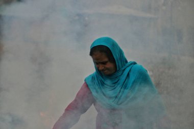 November 27,2023, Srinagar Kashmir, India : A Kashmiri woman burns dry chinar leaves in Srinagar. Kashmiris in these days collect dried leaves fallen from trees in order to burn them to produce charcoal to use as combustibles clipart