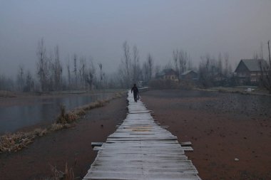 December 21,2023, Srinagar Kashmir, India : A man walks on a frost covered wooden bridge on a cold winter morning in Srinagar. The 40 day harshest winter period Chillai-Kalan, begins in Kashmir on Thursday clipart