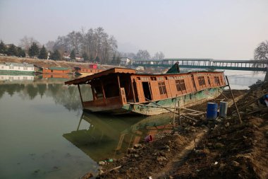 15 Ocak 2024, Srinagar Kashmir, Hindistan: Srinagar 'daki Jhelum nehrinin kıyısında alabora olmuş bir yüzen ev görüldü. Uzun süren Kurak Kış Büyüsü, Jhelum Nehri 'ni Alçak Tarihte Bırakıyor, Gulmarg' daki Yüzen Evleri ve Hayal kırıklığına uğratan Kayakçıları Tehlikeye Atıyor. 