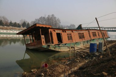 15 Ocak 2024, Srinagar Kashmir, Hindistan: Srinagar 'daki Jhelum nehrinin kıyısında alabora olmuş bir yüzen ev görüldü. Uzun süren Kurak Kış Büyüsü, Jhelum Nehri 'ni Alçak Tarihte Bırakıyor, Gulmarg' daki Yüzen Evleri ve Hayal kırıklığına uğratan Kayakçıları Tehlikeye Atıyor. 