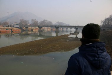 15 Ocak 2024, Srinagar Kashmir, Hindistan: Bir adam Srinagar 'daki Jhelum nehrinin kurumuş kısmına bakıyor. Uzun süren Kurak Kış Büyüsü, Jhelum Nehri 'ni Alçak Tarihte Bırakıyor, Gulmarg' daki Yüzen Evleri ve Hayal kırıklığına uğratan Kayakçıları Tehlikeye Atıyor