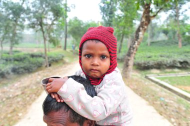 17 Ocak 2024 Sylhet-Bangladeş: Soğuk bir sabah Tarapur Çay Bahçesi 'nde gardiyanın kucağında bir çocuk. Sylhet 'te kış mevsiminin şiddetinin artması nedeniyle çocuklar ve yaşlılar acı çekiyor.