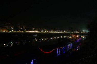 5 Mart 2024, Srinagar, Hindistan: Aydınlanmış bir yüzen ev Jhelum Nehri 'nin karşısında akşam saatlerinde Srinagar' da görülür.