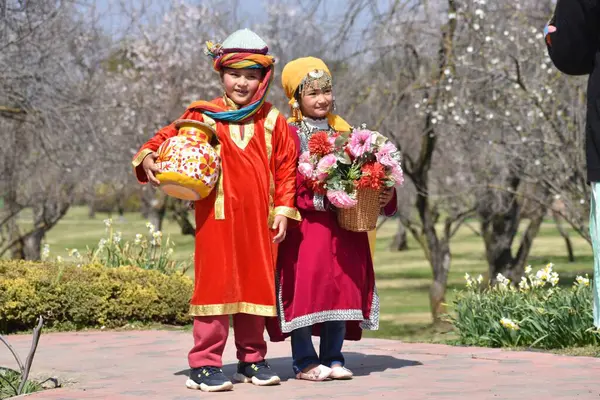 stock image March 20, 2024, Srinagar India: Two children are seen across the Almond blossom trees early spring across Badawari garden, the garden is very popular at the end of winter and the beginning of spring