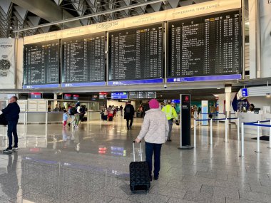 Havaalanında bereli yaşlı bir kadın uçuş kapısına bakmak için zaman çizelgesine bakıyor. Seyahat konsepti. Çantalı ve çantalı insanlar.. 