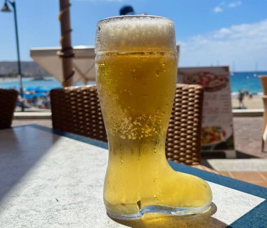 Açık hava kafesinin arka planında köpüklü altın lager içeceği olan çizme şeklindeki bira bardağı. Yüksek kalite fotoğraf