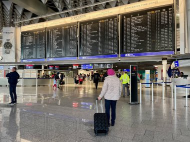 Havaalanında bereli yaşlı bir kadın uçuş kapısına bakmak için zaman çizelgesine bakıyor. Seyahat konsepti. Çantalı ve çantalı insanlar.. 