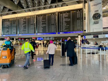 Havaalanında bereli yaşlı bir kadın uçuş kapısına bakmak için zaman çizelgesine bakıyor. Seyahat konsepti. Çantalı ve çantalı insanlar.. 