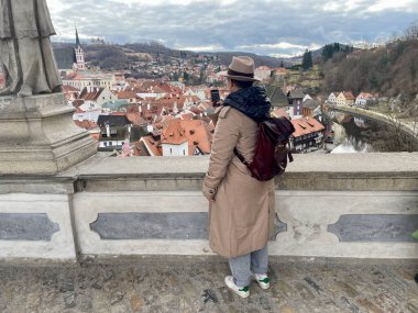 Sırt çantalı bir bayan turist, Cesky Krumlov 'un cep telefonuyla fotoğraflarını çekiyor. Eski bir peri masalı kasabası. Büyülü atmosfer ve muhteşem gökyüzü. Yüksek kalite fotoğraf. 