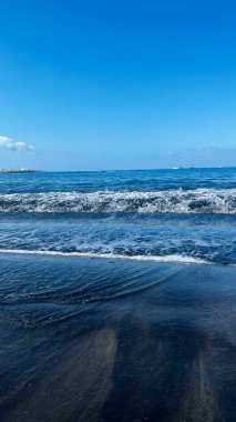 Atlantik dalgaları kumlu sahile vurdu. Siyah kum ve mavi gökyüzü. Dikey görüntü. Costa Adeje, İspanya. Yüksek kalite fotoğraf