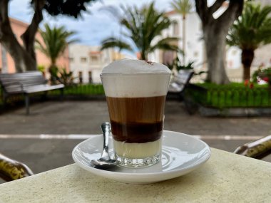 A horizontal selective of a barraquito shot on a table. In the background is the town of Garachico. High quality photo clipart