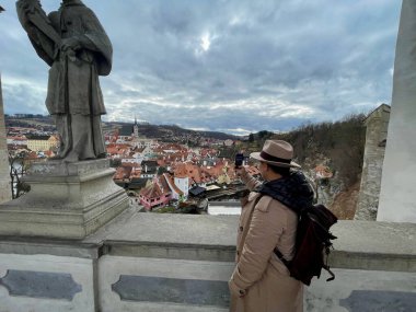 Sırt çantalı bir bayan turist, Cesky Krumlov 'un cep telefonuyla fotoğraflarını çekiyor. Eski bir peri masalı kasabası. Büyülü atmosfer ve muhteşem gökyüzü. Yüksek kalite fotoğraf. 