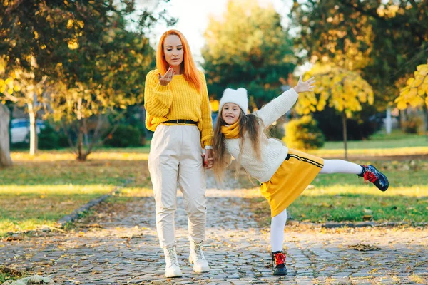 Stylish family on autumn walk. Happy mother and daughter walking in the park. Family enjoying the beautiful autumn nature. Mom and child having fun together. Autumn fashion, lifestyle.