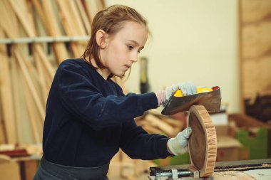 Young carpenter working with wood and sandpaper in craft workshop. School, development and learning concept. Cute boy makes wooden clock in the workshop.