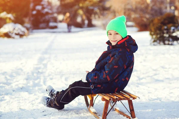 冬の公園で壊れた手を屋外で男の子 そりに座っている壊れた腕と石膏でかわいい子供 キャストを持ついたずら好きな子供 — ストック写真